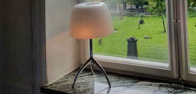Bild på bordslampa som står på en fönsterbänk, Lumiere bordslampa i krom och vit glasskärm från Foscarini